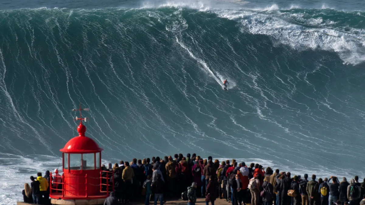 Massive waves crashing near the lighthouse cliff at Praia do Norte in Nazaré