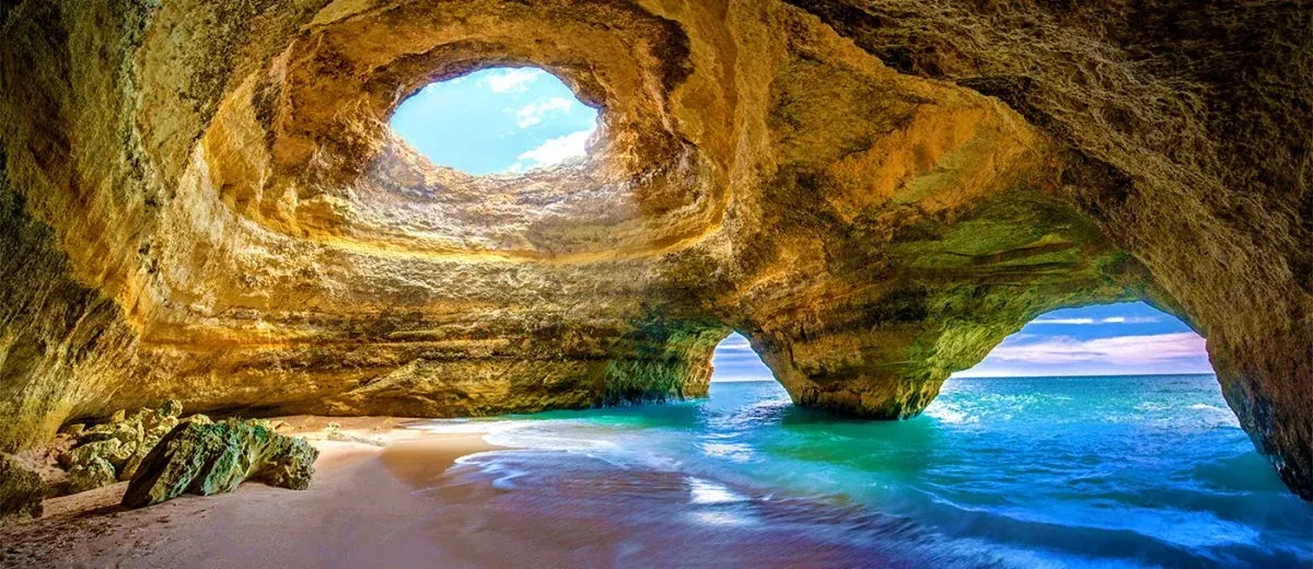 Inside the famous Benagil sea cave with a hole in the ceiling revealing the sky