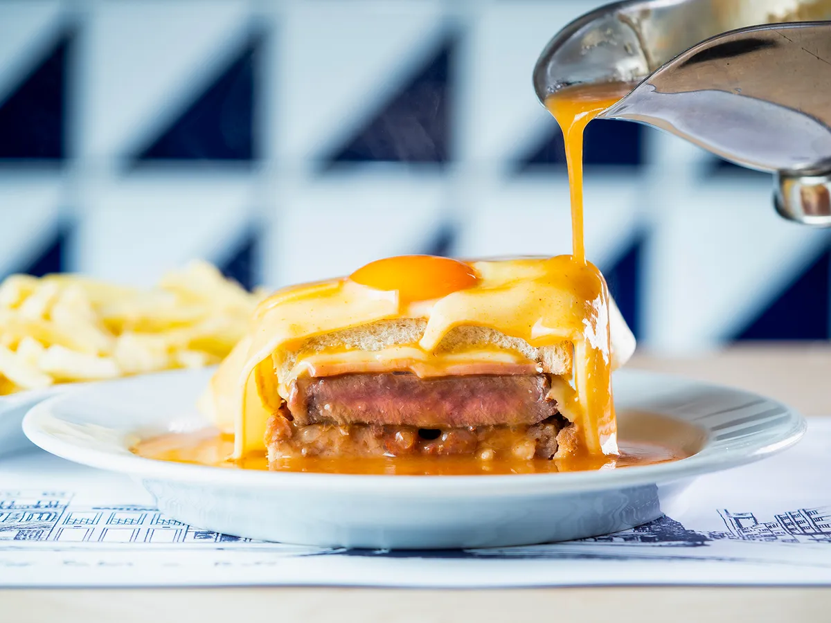 A traditional Porto Francesinha sandwich covered in melted cheese and hot sauce